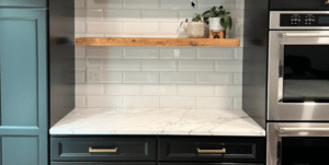 White marble countertop with wooden floating shelf and dark cabinets.