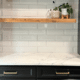 White marble countertop with wooden floating shelf and dark cabinets.