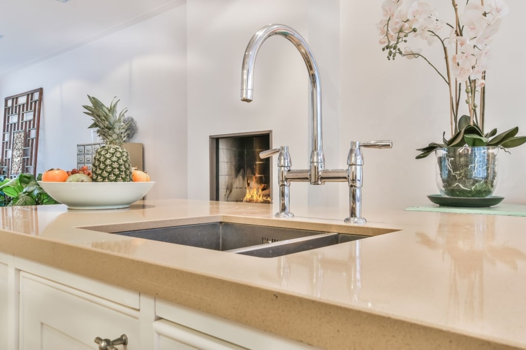 A warmly lit kitchen with sterling silver faucet and beautiful taupe quartz countertops.