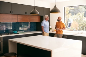 Senior Father Talking And Drinking Coffee With Adult Son In Kitchen At Home